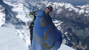 A mountaineer wrapped wearing the Queen's awards flag on the summit of a mountain.